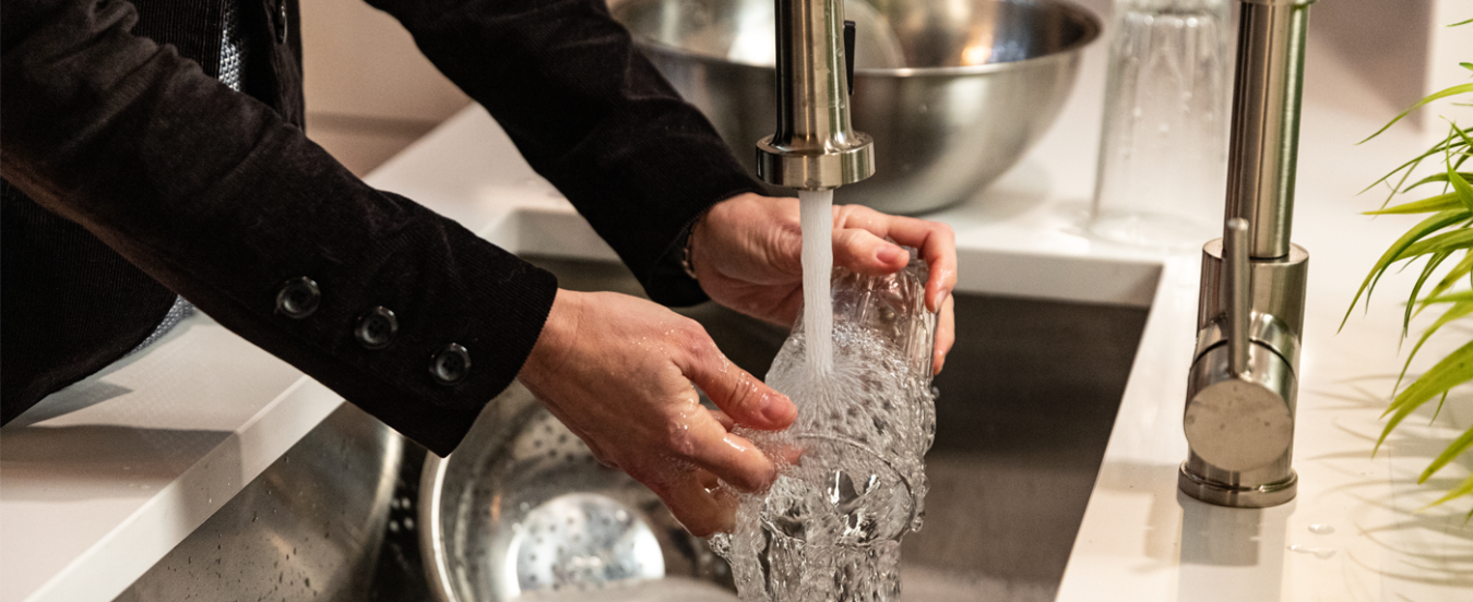Image of an adult washing a glass under running water in a kitchen sink.