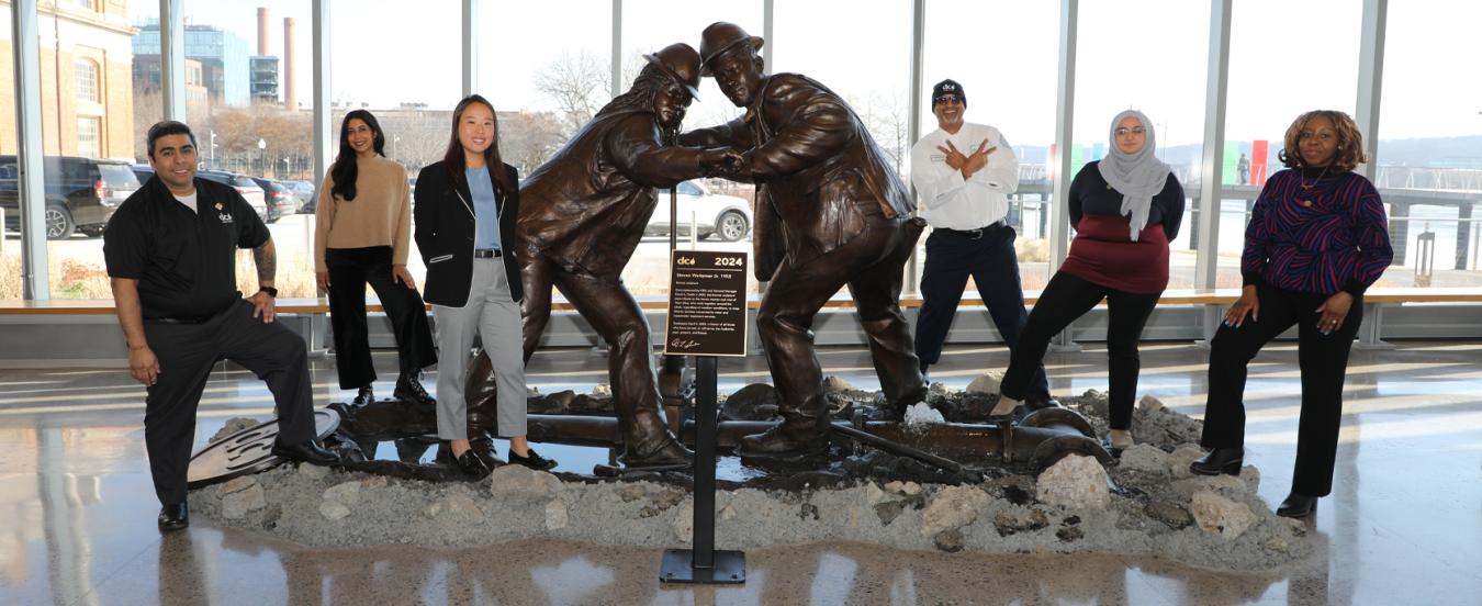 Six DC Water employees pose on either side of a new statue at DC Water.