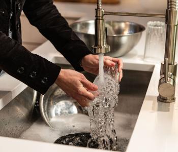 Photo shows an adult washing a glass in the sink with the faucet running.