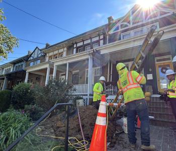 Photo of four workers at NW DC home replacing the lead service line. Worker brings a ladder in.