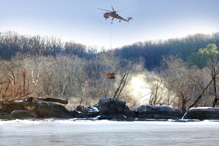 A helicopter lowers a drill rig to workers on the Potomac River.