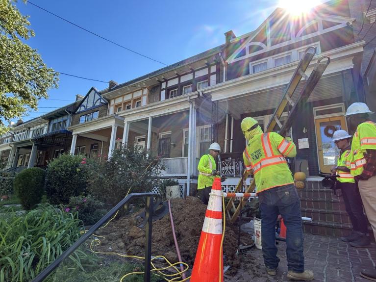 Photo of four workers at NW DC home replacing the lead service line. Worker brings a ladder in.