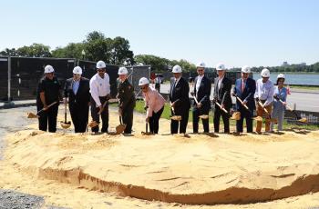 Speakers and other VIPs in hardhats lift dirt on their shovels during the ceremonial groundbreaking