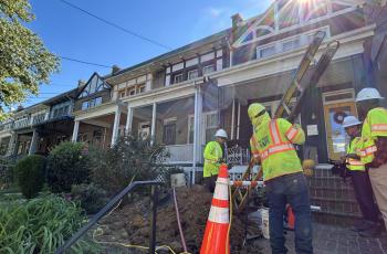 Photo of four workers at NW DC home replacing the lead service line. Worker brings a ladder in.